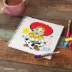 A coloring book page shows Jessie from Toy Story, colored in with markers. The page is on a wooden table next to a pink mug of hot chocolate and several colorful markers. Text on the page reads "Jessie.