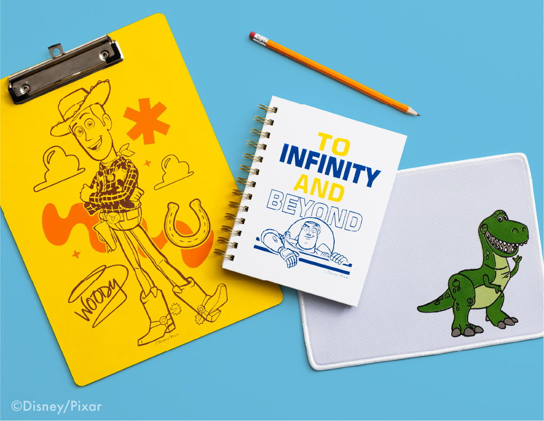 A yellow clipboard with a Woody sketch, a spiral notebook with "TO INFINITY AND BEYOND" and Buzz Lightyear, a pencil, and a white mat with a green dinosaur, all on a blue background.