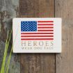 A wooden sign with an American flag above the gold text "Heroes wear dog tags," leaning against a rustic wooden background with green grass in the foreground.