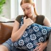 A woman with long red hair sits on a couch, eyes closed, hugging a blue decorative pillow with a white floral pattern. She appears relaxed and content.