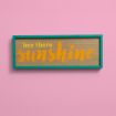 A wooden sign with a teal frame on a pink wall displays the text "hey there sunshine" in yellow and orange script.