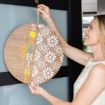 A woman hangs a round wooden sign decorated with white floral patterns and the words "hello SUNSHINE" in colorful letters, on a door.