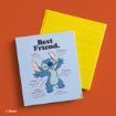 A blue photo album with Stitch from Disney’s "Lilo & Stitch" labeled “Best Friend.” Traits like “fluffy,” “energetic,” and “talented” are written around Stitch. A yellow album lies behind it on an orange surface.
