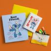 A flat lay of Stitch-themed stationery on an orange background, including a blue folder labeled "Best Friend," a spiral notebook, a pencil pouch with markers, and a yellow binder.