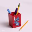 A red pen holder featuring Stitch from Disney’s “Lilo & Stitch” contains pens and a pencil. Another yellow pencil lies on the light surface next to the holder.