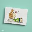 A cartoon girl with light brown hair, wearing a green and blue dress, lies on her back with her hands behind her head as a pink butterfly lands on her nose. The illustration is on a white rectangular card against a teal background.
