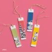 Four colorful rectangular bookmarks with cartoon dog illustrations, each with a twine loop, are arranged on a pink background. The bookmarks are decorated with different designs and bright colors.