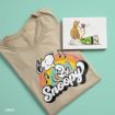 A beige T-shirt featuring Snoopy dancing with musical notes and a rainbow swirl design next to an illustration of a girl with a flower on her nose. Both items are on a light green background.