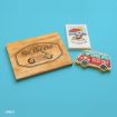 A wooden plaque with "Rad Dad Club" and a motorcycle, a small card with Snoopy under an umbrella labeled "The Good Life," and a decorated cookie shaped like a van with "Road Trip" on a blue background.