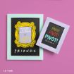 Two framed chalkboard-style prints on a pink background. One says "Welcome to the real world" and "FRIENDS" with a yellow frame, the other says "PIVOT! PIVOT! PIVOT! FRIENDS" in colorful text.