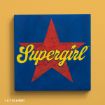 A blue square canvas featuring a large red star in the center with the word "Supergirl" written in yellow cursive text across it, set against a solid yellow background. © & ™ DC & WBEI.