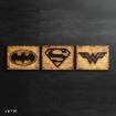 Three wooden plaques feature black logos of Batman, Superman, and Wonder Woman, arranged side by side against a dark background. The Batman logo is on the left, Superman in the center, and Wonder Woman on the right.
