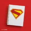 A white spiral notebook with a red and yellow Superman logo on the cover is placed on a bright red background. DC & WBEI copyright text is visible in the lower left corner.
