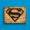 A wooden plaque featuring the iconic black Superman "S" shield logo on a yellowish-brown background, set against a bright blue wall. © & ™ DC.