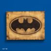 A wooden plaque with a black Batman logo in the center, featuring a bat silhouette inside an oval. The plaque has a slightly burnt, rustic look and is mounted on a solid blue wall. DC copyright is visible in the corner.