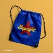 A blue drawstring bag with black strings, featuring a large red star and the yellow word "Supergirl" on the front, placed on a yellow surface. DC & WBEI copyright text is in the bottom left corner.