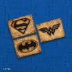 Three wooden plaques with black logos of Superman, Wonder Woman, and Batman are displayed on a blue background with faint superhero-themed words and symbols.
