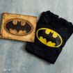 A black hoodie with a yellow Batman logo next to a wooden plaque featuring a burned-in Batman logo, both placed on a textured blue surface.