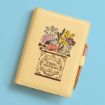 A yellow journal with a floral illustration and the words "Calm the Frick Down" on the cover, resting on a light blue surface with a pen attached to the journal.