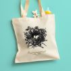 A beige tote bag with a black nest and eggs illustration, and the words "Every good and perfect gift is from above. James 1:17." A baby bottle and small teddy bear are tucked into the bag, set against a teal background.