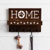 A wooden wall rack with "HOME" written on it, the "O" replaced by a paw print. The rack has five hooks holding a rope toy and a leash, with small paw prints and dog treats on the shelf above the hooks.