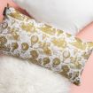 A rectangular pillow with a gold hot air balloon and landscape pattern on white fabric rests on a fluffy white rug, next to a plain white pillow, all set on a pale pink background.