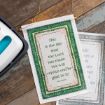 A decorative fabric sign on a wooden surface displays the Bible verse Psalm 118:24: "This is the day that the Lord has made. We will rejoice and be glad in it." The sign is bordered with green and floral patterns.