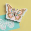 A butterfly-shaped card with decorative brown, pink, and teal patterns sits on a yellow surface next to a turquoise card featuring a white butterfly outline with similar designs.