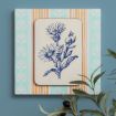A framed botanical illustration of blue flowers hangs on a blue wall with mint green and orange striped wallpaper. Part of a leafy plant with olives is visible in the lower right corner.