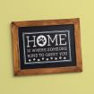 A framed sign on a yellow wall reads "Home is where someone runs to greet you," with a paw print in place of the "O" in "Home" and a row of small paw prints along the bottom.
