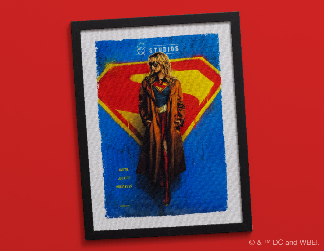 Framed poster of a woman in a trench coat and Supergirl costume standing in front of a large Superman symbol, with a blue and yellow background on a red wall. The words "Truth. Justice. Whatever." appear on the left.