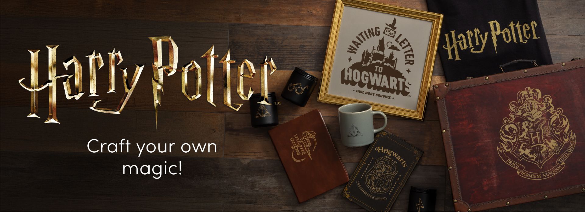 A collection of Harry Potter-themed merchandise, including a framed Hogwarts letter print, a notebook, mugs, tumblers, and a trunk, arranged on a wooden surface with the text "Harry Potter Craft your own magic!.