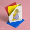 A white organizer box with an illustration of Rapunzel in a purple dress holds colorful paper sheets—red, yellow, and blue—on a pink background. Blue sheets are also placed on the surface nearby.