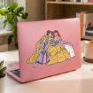 A pink laptop with a sticker of three Disney princesses—Rapunzel, Belle, and Ariel—reading books together, placed on a desk with books, a plant, and a cup in the background.