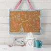 A framed corkboard with pastel sketches of Disney princess-themed icons hangs on a white wall above a desk with a framed quote, blue mug, tissue box, and pastel-colored pens.