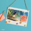A rectangular board with a Moana scene, four colorful magnets, a sticky note reading "Lunch @ 12.30 :)", a pencil, and a stack of sticky notes, all on a blue background. © Disney.