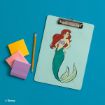 A clipboard with an illustration of Ariel, the mermaid from Disney's "The Little Mermaid," sits on a blue surface next to a yellow pencil and three square sticky note pads in yellow, pink, and purple.