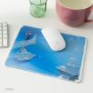 A Disney-themed mouse pad featuring Cinderella running down blue stairs, with her glass slipper left behind. A white wireless mouse and keyboard sit nearby, next to a pink mug and a green glass.