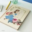 A spiral notebook features an illustration of Belle from Disney's Beauty and the Beast, surrounded by roses, on a wooden cover. The notebook is on a desk with a pencil, keyboard, and glass bottle nearby.