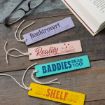 Four colorful bookmarks on a wooden surface, each with a different phrase: “Booktrovert,” “Reality can wait,” “Baddies read too!,” and “I have no shelf control.” Glasses and an open book are nearby.