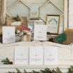 A festive display features wrapped gifts, pinecones, greenery, and framed holiday decor on a white mantel. Four cards with gold stars and Bible verses are arranged in front, each with a different title for Jesus.