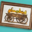 Framed illustration of a wooden cart filled with various pumpkins and gourds, set against a turquoise background. The drawing has a rustic, vintage style with warm brown and orange tones.