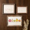 Three framed autumn-themed prints hang on a wooden wall; two have seasonal words, and one shows five illustrated gourds in fall colors above the words “chilly nights.” Dried grasses rest below the frames.