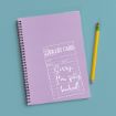 A lavender spiral notebook with a mock library card design on the cover reads “Sorry, I’m fully booked!” A yellow pencil with a pink eraser lies next to it on a light blue surface.