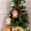 A Christmas tree decorated with red, green, and gold ornaments, and three snow globe-shaped snowman ornaments. Wrapped gifts with gold bows are placed under the tree, set against a white wooden wall.