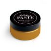 A round container of Chalkology Paste by Chalk Couture with a black lid and mustard yellow paste inside, labeled as washable paste.