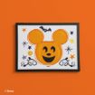 Framed art of a pumpkin shaped like Mickey Mouse’s head, with a happy face, surrounded by stars, swirls, and a bat, set against an orange background.