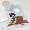 A white desk with a keyboard, mouse, and a drink, featuring a mat with Mickey Mouse in autumn clothes next to a basket of pumpkins and leaves.