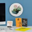 A desk with a computer, mouse, notepad, and Disney-themed stationery sits below a wall clock featuring a green abstract Mickey Mouse design.
