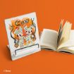 A book stand displays Disney art of Mickey and Minnie as mummies with pumpkins, next to an open book standing on an orange surface.